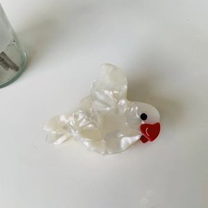 Detail view of a pearlescent white acetate bird hair claw with red beak on white background