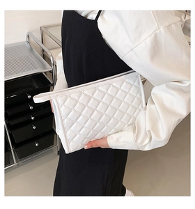 Detail of white quilted cosmetic bag with diamond lattice pattern and side handle strap