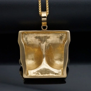 Macro shot of gold-plated abstract female torso pendant on reflective black background