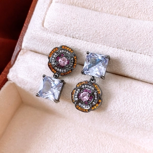 Macro shot of asymmetric flower earrings with pink and orange gemstones in a jewelry box