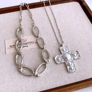 Detailed top view of silver cross pendant necklaces with pearls on a wooden tray