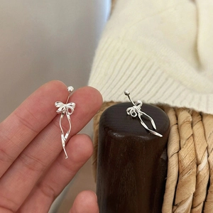 Elegant silver bow ribbon earrings with metallic texture shown against a warm wooden background