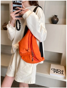 Detail of bright orange crossbody bag featuring multi-layer zippers and wide nylon strap