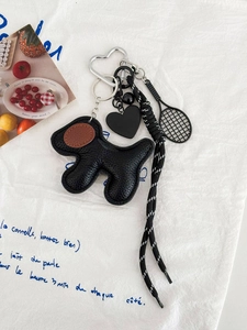 Detail of leather puppy keychain with black heart and tennis racket on a textured cloth