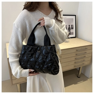 Close-up of black quilted puffer tote bag with wide webbing handles held by a model