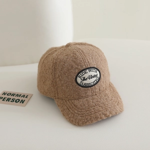 Detailed close-up of camel fleece baseball cap with vintage embroidery on white surface
