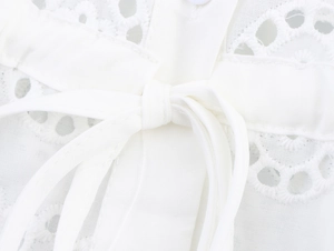 Detail view of French-style white eyelet lace blouse featuring a lace-up bow and embroidery