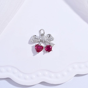 Macro detail of cherry-shaped bow pendant with red heart gems and sparkling silver setting