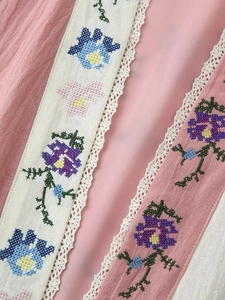 Dettaglio macro di ricami floreali colorati e pizzo bianco delicato su tessuto rosa