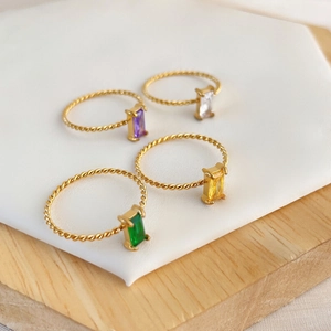 Detail of four colorful gemstone rings with twisted gold bands on display stand