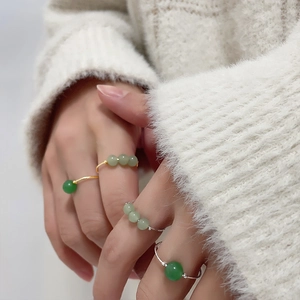 Detailed view of stackable gold and silver wire rings with green beads on finger