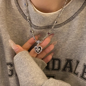 Detail of silver heart necklace with cross relief and purple beads on apparel