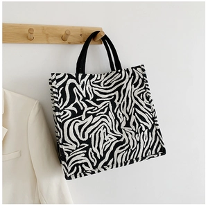 Detail of zebra print tote bag hanging on wooden hook with stylish white blazer