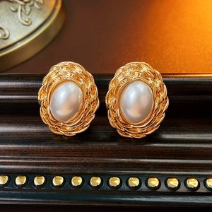 Close-up of vintage oval pearl earrings with gold woven texture frames on wood