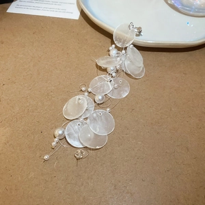 Detail of elegant long tassel earrings with white pearl and shell discs on textured background