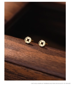 Macro shot of gold-plated sterling silver coin earrings on a textured wooden surface