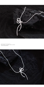 Close-up of silver ribbon bow pendant necklace on dark textured charcoal background
