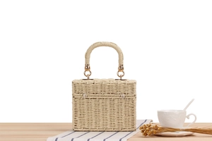 Detail of a beige woven box handbag with round handles on a rustic wooden table