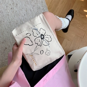 Detail of floral embroidery on a cream canvas cosmetic bag held by a model