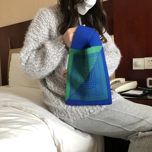 Blue and green knitted tote bag with geometric patterns shown by a model on a bed