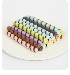 Close-up of colorful striped PVC wafer rolls and chocolate sticks on a white plate