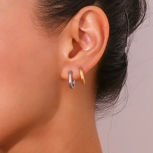Close-up of minimalist gold and silver huggie hoop earrings shown on a model ear