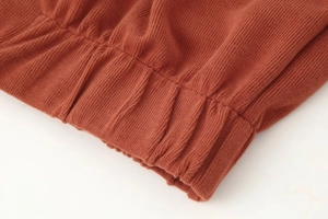 Makro-Detail des ziegelroten Rippstrickgewebes mit elastischen Bündchen und feiner Naht