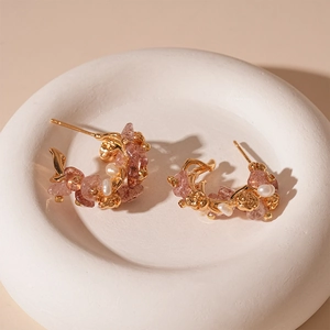 Close-up of golden C-shaped earrings with pink crystals and small white pearls on a tray