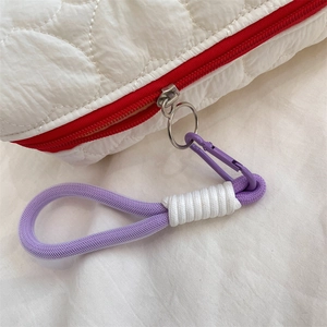 Close-up of white quilted cosmetic bag with red zipper and purple braided wristlet strap