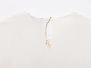Detail view of cream pleated top with back teardrop cutout and single button lace closure