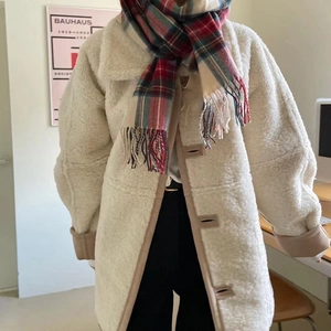 Close-up of a festive red plaid scarf with tassels paired with a beige sherpa fleece coat
