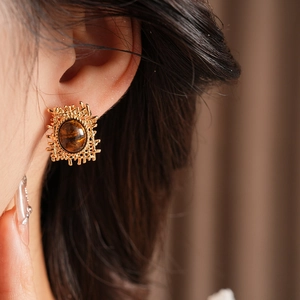 Close-up of a gold woven square earring with brown tiger eye stone on model's ear