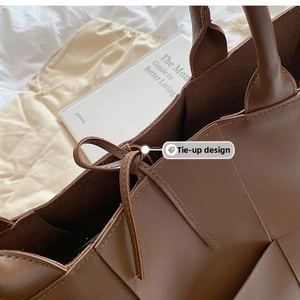 Detail of a brown woven tote bag showing the lace-up tie closure and leather texture