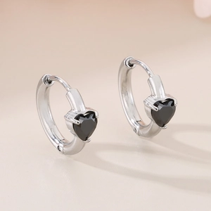 Detail of silver heart hoop earrings with black stones on a soft beige background