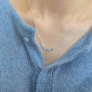 Close-up of minimalist silver leaf pendant with hammered texture on a female model