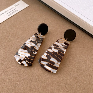 Detail of geometric resin earrings with black and yellow patterns and gold accents