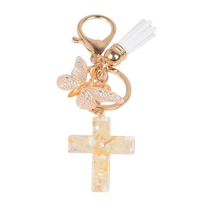 Close-up of resin cross keychain with golden butterfly and white tassel on white background