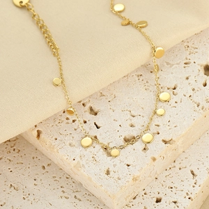 Detail of a gold plated necklace with small disc charms on a textured stone base
