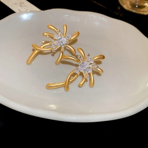 Close-up of matte gold firework stud earrings with sparkling white zircons in a ceramic dish