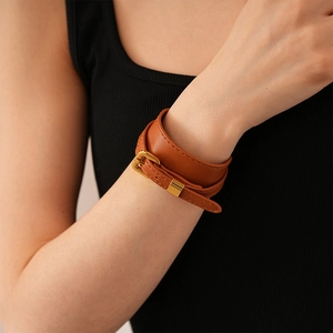 Macro detail of dark brown faux leather wrap bracelet with golden metal buckle clasp