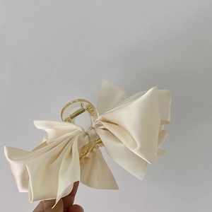 Detail view of large cream satin bow hair claw clip with elegant silk texture and sturdy spring