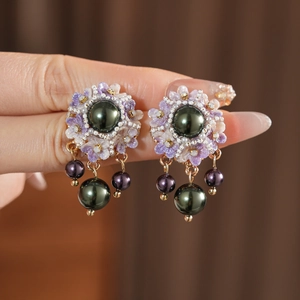 Macro shot of purple floral pearl earrings featuring green pearls held by hand