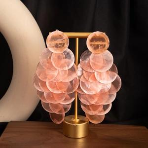 Detailed view of layered pale pink shell petal drop earrings on a golden display stand