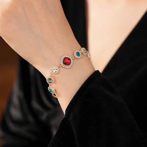 Close-up of model wearing gold bracelet with colorful rhinestones on a dark background