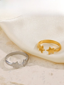 Detailed close-up of 18K gold and silver star rings on beige satin and stone
