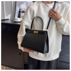 Close-up of black leather crossbody bag with golden square lock worn by a model