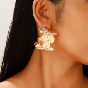 Close-up of model wearing large golden flower petal earrings with metallic luster