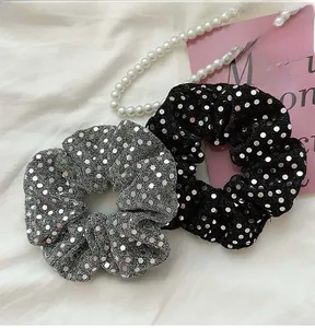Detail of silver and black sequin hair scrunchies on white fabric with pearl decor