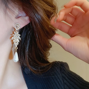 Close-up of golden leaf rhinestone earrings with teardrop pearl on a model's ear