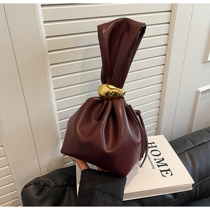 Detail of burgundy leather bucket bag with twisted handle and gold metal ring accent